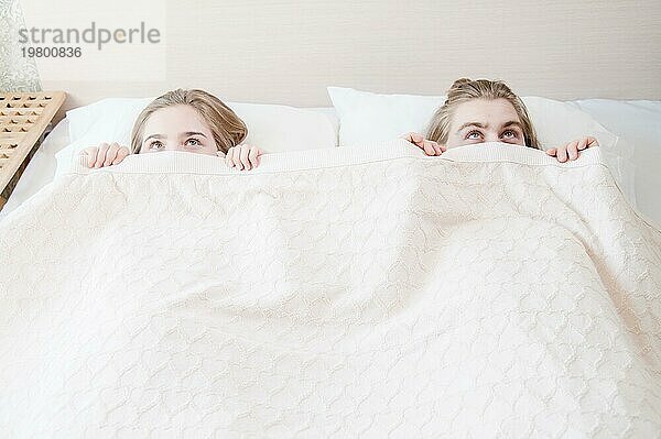 Ein junges Paar im Bett bedeckt die Hälfte seines Gesichts mit einer Decke und versteckt sich hinter einer Decke. Das Konzept der familienfreien Probleme und des Mangels an Dialog