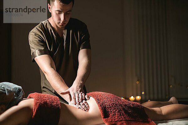 Kosmetologie und Physiotherapie. Professionelle Massage auf den unteren Rücken einer Frau wird von einem Masseur Mann gemacht. Konzept der manul Therapie und Massage Spabehandlungen