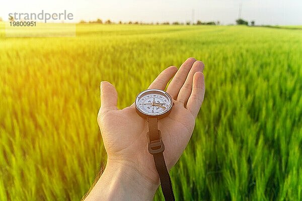 Orientierungssuche in der Natur auf einem Weizenfeld. Die Hand eines Mannes hält einen Kompass