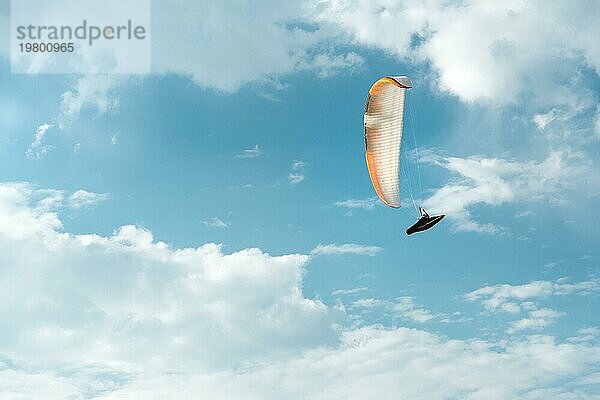 Professioneller Gleitschirmflieger fliegt mit einem weißen Gleitschirm gegen den blaün Himmel und die weißen Wolken. Gleitschirmfliegen Sport