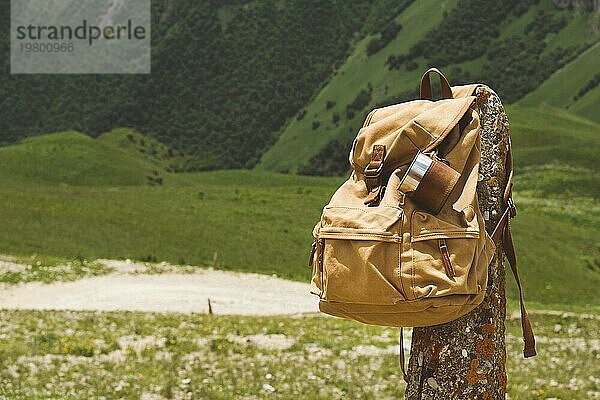 Hipster gelben Vintage Rucksack mit einem Becher auf sie mit einem Becher Nahaufnahme Vorderansicht befestigt. Traveler's Reisetasche im Hintergrund einer Berglandschaft