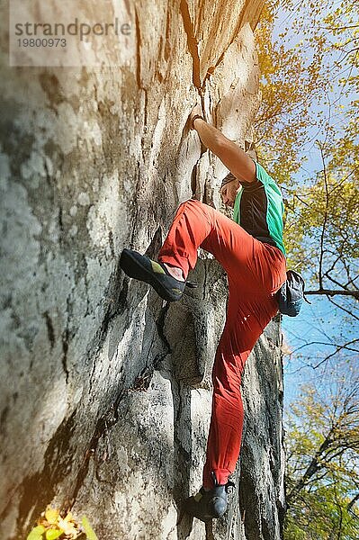 Ein bärtiger Mann  der mit einem Beutel Magnesia und Kletterschuhen gealtert ist  wird auf einem nicht hohen Felsen im Wald trainiert. Training von Kletterern unter natürlichen Bedingungen