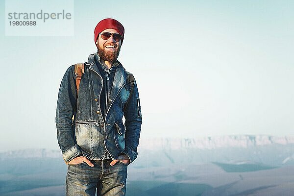 Hipster junger Mann mit Bart und Schnurrbart und Sonnenbrille posiert vor dem Hintergrund der Berge