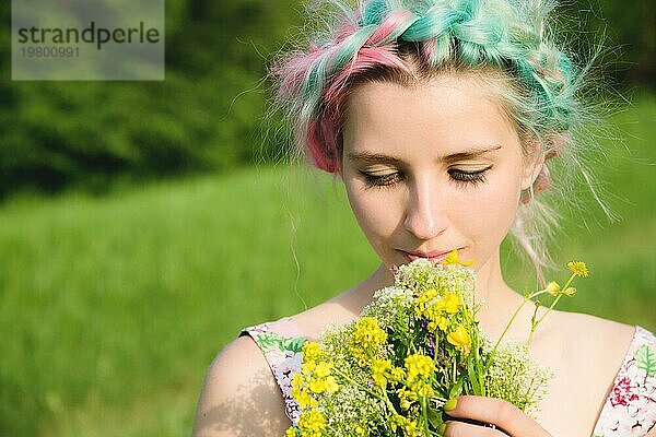 Porträt eines jungen  glücklich lächelnden Mädchens in einem Baumwollkleid mit einem Strauß Wildblumen