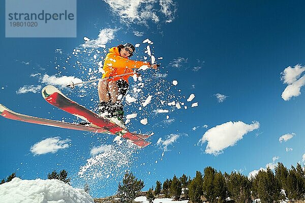 Mann Skifahrer im Flug nach dem Sprung von einem Kicker im Frühjahr vor dem Hintergrund der Berge und blaün Himmel. Nahaufnahme mit Weitwinkel. Das Konzept der Schließung der Skisaison und Skifahren im Frühjahr