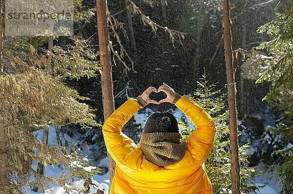 Rückenporträt junge kaukasische Frau und zeigt Finger Geste des Herzens  Liebe auf Augenhöhe. Rückenansicht in Wald und Bergen. Rückenansicht