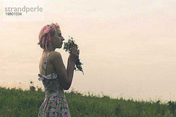 Junge Frau im Kleid mit Blumenstrauß in den Händen bei Sonnenuntergang auf einem Feld. Getöntes kaltes Bild