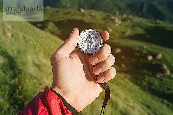 Mann auf der Suche nach der Richtung mit einem Kompass in der Hand in den Sommerbergen. View Point auf dem Hintergrund der grünen Hügel und Gras. Richtungssuche