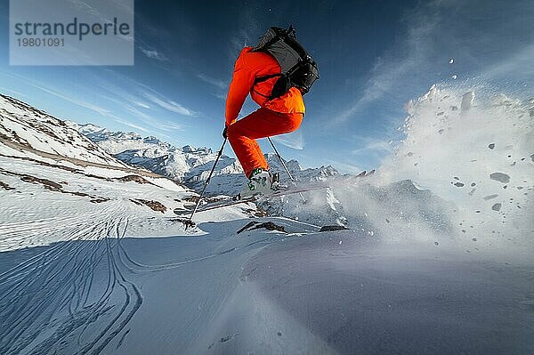 Großaufnahme Ein männlicher Skifahrer springt von einem schneebedeckten Hang vor dem Hintergrund einer Berglandschaft mit schneebedeckten Bergen an einem sonnigen Tag. Das Konzept des Wintersports