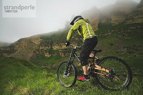 Ein Mann mit Berghelm und Mountainbike fährt bei bewölktem Wetter durch die schöne Natur bergab