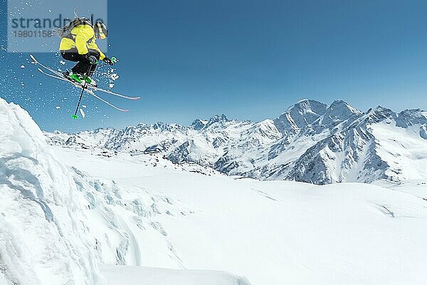 Ein Skifahrer in voller Sportausrüstung springt von der Spitze des Gletschers in den Abgrund vor dem Hintergrund des blaün Himmels und der schneebedeckten Berge des Kaukasus. Elbrus Gebiet. Russland