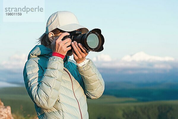 Porträt einer Fotografin mit Mütze in der Natur beim Fotografieren mit ihrer digitalen Spiegelkamera. Vorderansicht