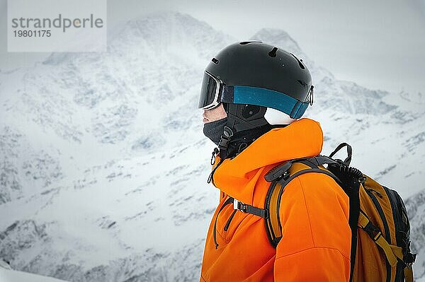 Porträt eines jungen Erwachsenen mit Skihelm und Skibrille  mit hohen verschneiten Bergen im Hintergrund