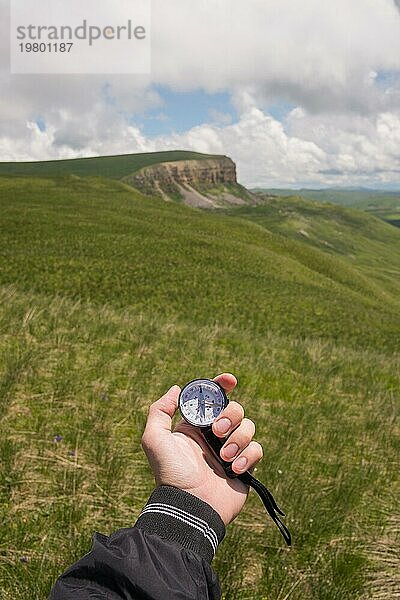 Männliche Hand eines Touristen mit einem echten Kompass vor dem Hintergrund einer Berglandschaft