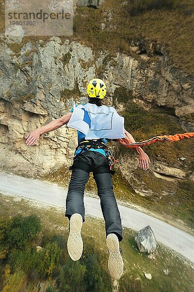 Ein Mann mit Helm springt mit einer leeren Flagge in den Bergen Seil hoch. Extremsportarten. Freizeit. Ansicht von oben