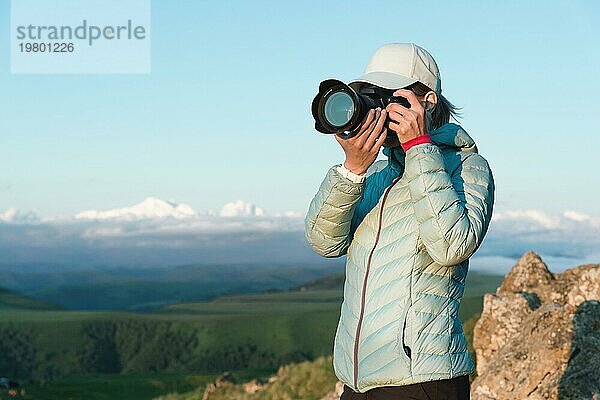 Porträt einer Fotografin mit Mütze in der Natur beim Fotografieren mit ihrer digitalen Spiegelkamera. Vorderansicht