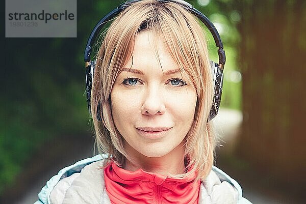 Attraktive blonde Frau im Wald. Nahaufnahme eines sportlichen lächelnden Mädchens beim Musikhören