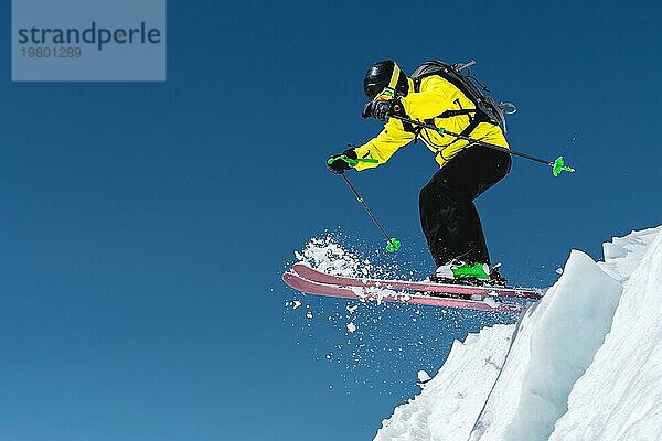 Ein Skifahrer in voller Sportausrüstung springt von der Spitze des Gletschers in den Abgrund vor dem Hintergrund des blaün Himmels und der schneebedeckten Berge des Kaukasus. Elbrus Gebiet. Russland