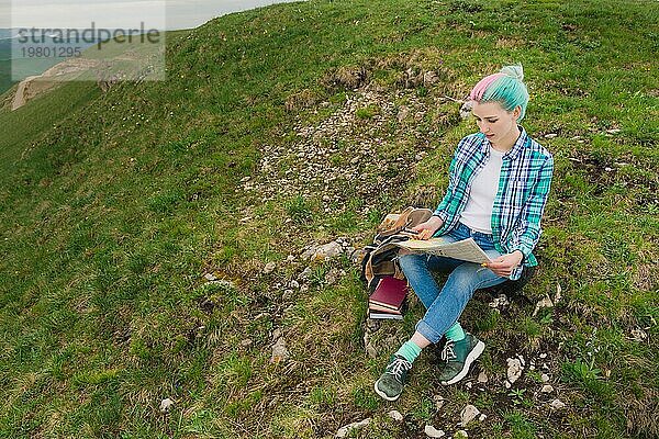 Mädchen Reisende mit bunten Haaren sitzen auf Natur Lesekarte und hält einen Kompass in der Hand. Das Konzept der Navigation der Suche und Tourismus in den Bergen. Reisen Konzept