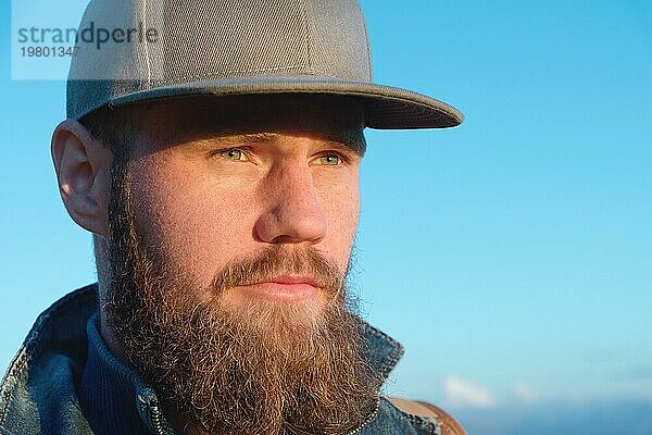 Close up Porträt eines bärtigen stilvollen Reisenden mit Mütze vor blauem Himmel. Zeit zum Reisen Konzept