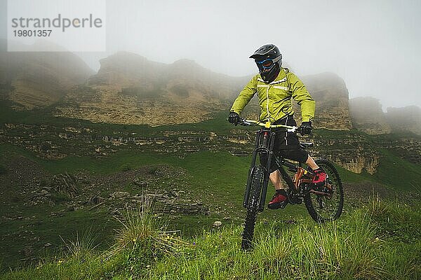 Ein Mann mit Berghelm und Mountainbike fährt bei bewölktem Wetter durch die schöne Natur bergab