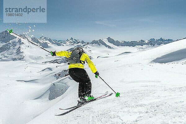 Ein Skifahrer in voller Sportausrüstung springt von der Spitze des Gletschers in den Abgrund  vor dem Hintergrund des blaün Himmels und der schneebedeckten Berge des Kaukasus. Blick von hinten. Elbrus Gebiet. Russland