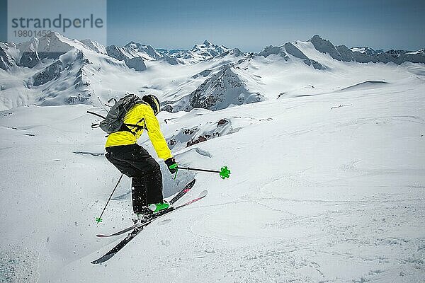 Ein Skifahrer in voller Sportausrüstung springt von der Spitze des Gletschers in den Abgrund  vor dem Hintergrund des blaün Himmels und der schneebedeckten Berge des Kaukasus. Blick von hinten. Elbrus Gebiet. Russland