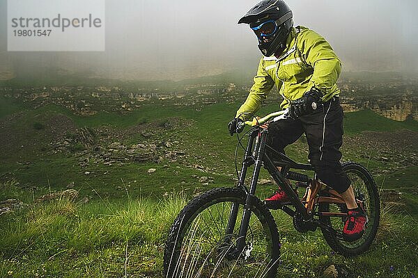 Ein Mann mit Berghelm und Mountainbike fährt bei bewölktem Wetter durch die schöne Natur bergab