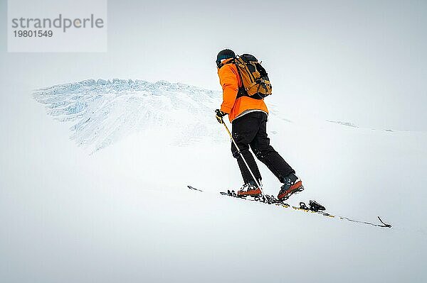 Winterskitour bei bewölktem Wetter  schneebedeckte Berge vor der Kulisse eines Gletschers. Skifahrer Mann in voller Ausrüstung klettert bergauf in einer Skitour