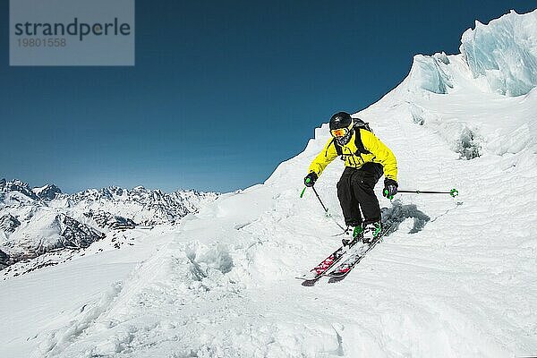 Professioneller Skifahrer bei der Geschwindigkeit vor dem Sprung vom Gletscher im Winter gegen den blaün Himmel und die Berge