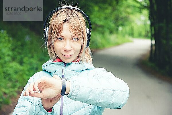 Porträt Junge Fitnessfrau schaut auf ihre Smartwatch  während sie eine Pause vom Sporttraining macht. Sportlerin prüft Puls auf Fitness Smartwatch Gerät im Wald