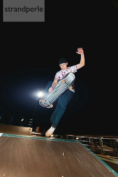 Ein junger Skater vollführt den Trick des nächtlichen Gleitens in einem Skatepark inmitten der brennenden Lichter der Lichtmasten