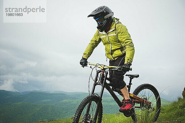 Ein Mann mit Berghelm und Mountainbike fährt bei bewölktem Wetter durch die schöne Natur bergab