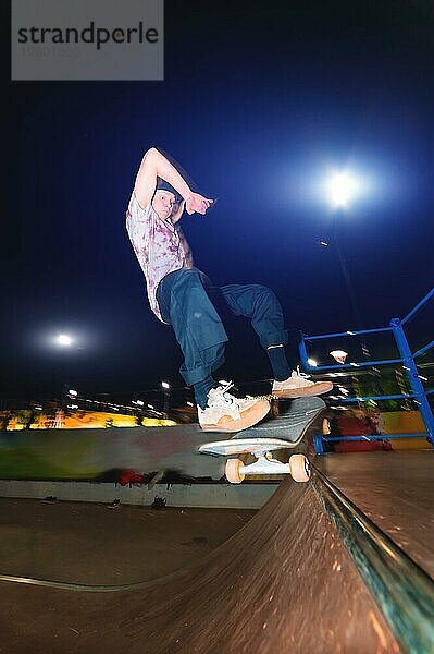 Ein junger Skater vollführt den Trick des nächtlichen Gleitens in einem Skatepark inmitten der brennenden Lichter der Lichtmasten