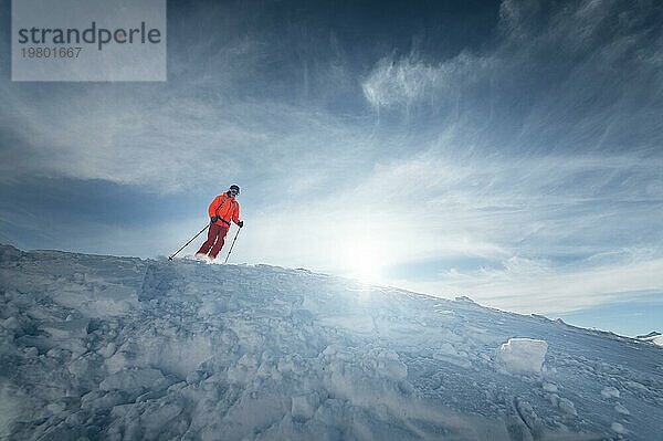 Ein männlicher Skisportler springt an einem sonnigen Tag von einem schneebedeckten Hang vor dem Hintergrund einer Berglandschaft mit schneebedeckten Bergen. Das Konzept des Wintersports