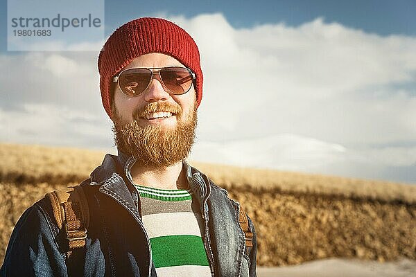 Porträt eines jungen Hipster Mannes mit Sonnenbrille und Hut. Ein lächelnder  bärtiger Mann mit Sonnenbrille. Glücklicher Mann mit Bart