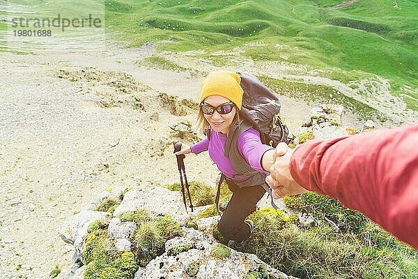 Ein Bergsteiger hilft einer jungen Bergsteigerin  den Gipfel des Berges zu erreichen. Ein Mann reicht einer Frau eine helfende Hand. Blick von oben