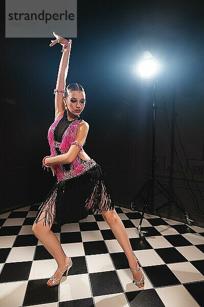 Junge attraktive Mädchen in einem schwarzen rosa Kleid in einem dunklen Raum Studio tanzt lateinamerikanische Tänze. Professionelle Tänzerin von Ballsaal Sport tanzen