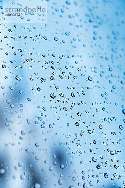 Vertikale Aufnahme. Geringe Schärfentiefe Wassertropfen auf Glas bei regnerischem Wetter mit unscharfen Schlafplätzen in einer Kleinstadt im Hintergrund. Herbst kalten naßen Hintergrund