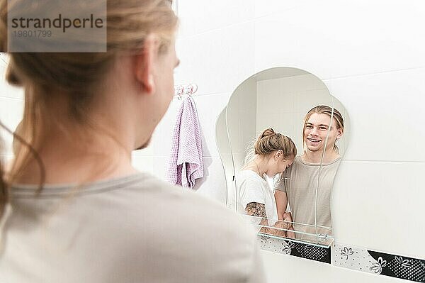 Junges heterosexuelles Paar lacht vor dem Badezimmerspiegel am Morgen
