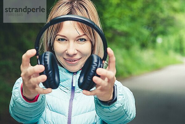 Glückliches Mädchen im Freien im Wald hält Kopfhörer. Das Konzept der Stereo Musik überall. Wandernde Musik