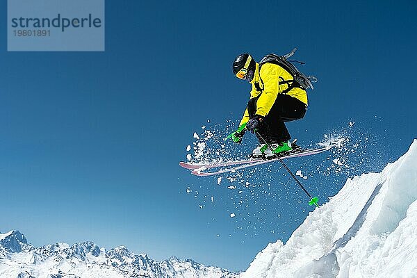 Ein Skifahrer in voller Sportausrüstung springt von der Spitze des Gletschers in den Abgrund vor dem Hintergrund des blaün Himmels und der schneebedeckten Berge des Kaukasus. Elbrus Gebiet. Russland