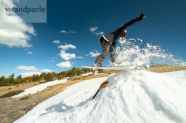 Stylish junges Mädchen Snowboarder macht den Trick beim Springen von einem Schnee Kicker gegen den blaün Himmel Wolken und Berge im Frühjahr. Das Konzept der Frühling Snowboarden in den Bergen und die Schließung der Winter Ski Saison