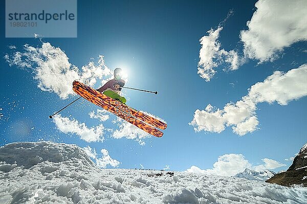 Eine Skifahrerin macht einen Sprungtrick und verdeckt dabei die Sonne. Fliegender Skifahrer vor dem Hintergrund des Himmels und der Wolken