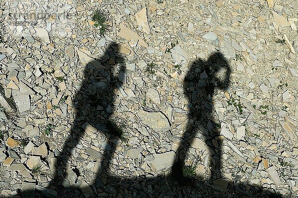 Zwei Schatten von Fotografen auf der Erde  die bergauf gehen. Silhouetten von zwei Menschen zu Fuß bergauf