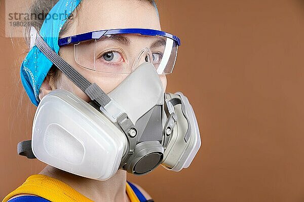 Porträt einer jungen kaukasischen Frau in Schutzausrüstung für die Seh und Atmungsorgane. Blick in die Kamera. Ein Mädchen mit Atemschutzmaske und Schutzbrille in einem Arbeitsanzug. Studioaufnahme