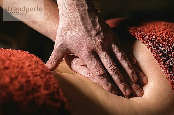 Kosmetologie und Physiotherapie. Professionelle Massage auf den unteren Rücken einer Frau wird von einem Masseur Mann gemacht. Konzept der Manultherapie und Massage Spa Behandlungen. Nahaufnahme