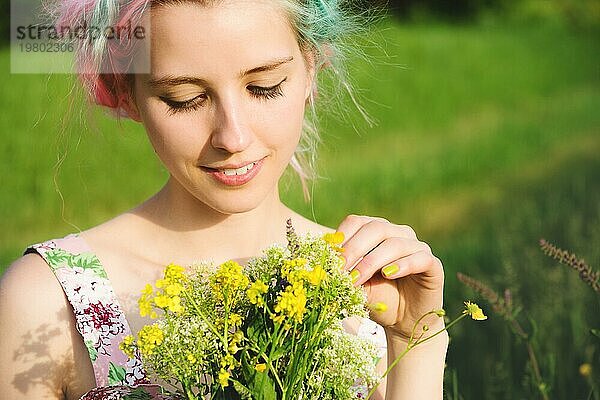 Porträt eines jungen  glücklich lächelnden Mädchens in einem Baumwollkleid mit einem Strauß Wildblumen