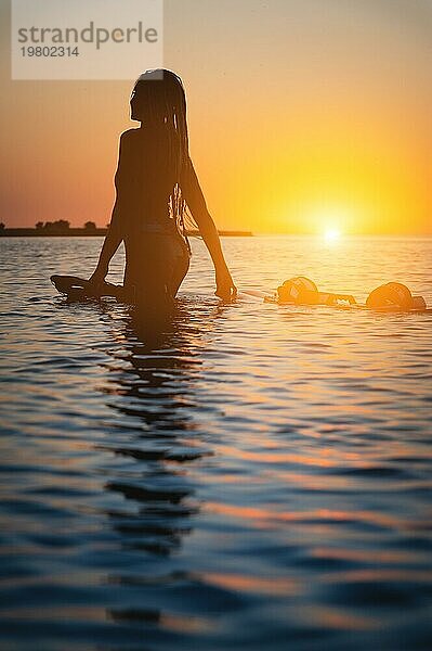 Silhouette einer schlanken jungen Athletin Kitesurfer schwimmt bei Sonnenuntergang im Meer neben ihrem Kite Board