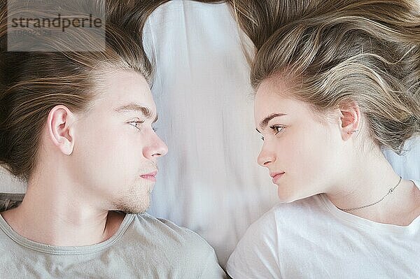 Draufsicht Porträt langhaariges Paar von Männern und Frauen  die auf dem Bett liegen und sich gegenseitig anschauen. Das Konzept von gesundem Sex und Glück in jungen Familien